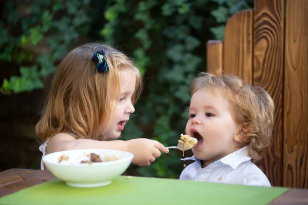 Schattig baby kind eet voedsel, baby 's eten. Klein meisje zus voeden baby. — Stockfoto