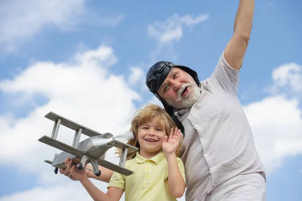 Grand-père drôle et fils jouant avec avion en bois sur fond de ciel d'été. Enfant garçon avec des rêves de voler ou de voyager. Famille générationnelle. — Photo