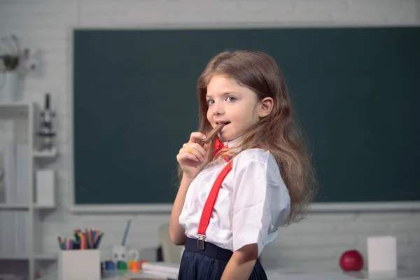 Bambino carino mangiare caramelle al cioccolato a scuola. Il ragazzo sta imparando in classe sullo sfondo della lavagna. — Foto Stock