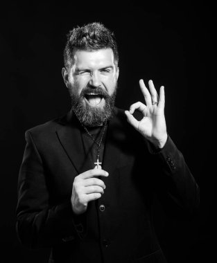 Beyaz arka plan üzerinde duran rahip üniforması giyen genç adam el hareketleriyle gülümsüyor ve mutlu yüzle parmaklarının arasından bakıyor..