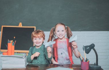 Okula geri dön ve mutlu zaman. Komik küçük çocuk tahta arka planda eğlenmek. Sınıf dostu çocuk tahta masası yakın kağıt uçak ile oynamak.