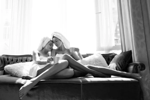 Sensual lésbicas namoradas. Jovens mulheres sexy bonitas em roupões de banho brancos e toalhas no quarto. Modelos femininos despreocupados na cama em apartamento ou quarto de hotel. Descanso da manhã. — Fotografia de Stock