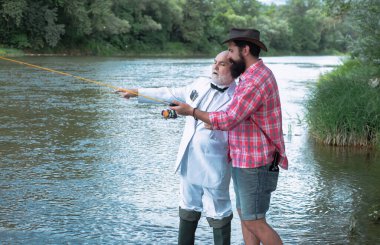 Baba oğlu ile nehirde balıkçılık balıkçılık balıkçılık zevk oltaları tutarak. Balıkçı -lık. Nehirde olta sıyrık olan balıkçılar. Mutlu aile kavramı - baba ve oğul birlikte.