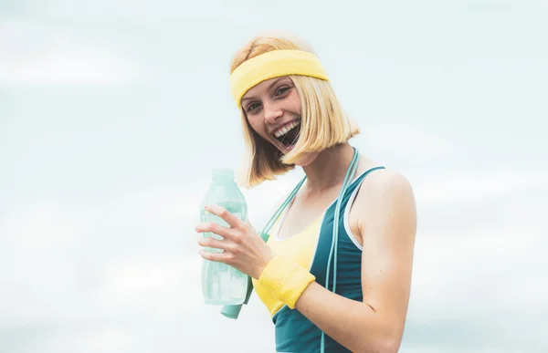 Athlète joyeuse joyeuse joyeuse regardant avec confiance dans la caméra tout en tenant une bouteille d'eau, portant des vêtements jaune-bleu s'entraînant dans la rue . — Photo