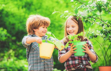 Kırsal kesimdeki çiftlikte yaşayan mutlu çocuk çiftçileri. Şirin küçük oğlan ve kız bahar günü bahçede çiçek suluyorlar..