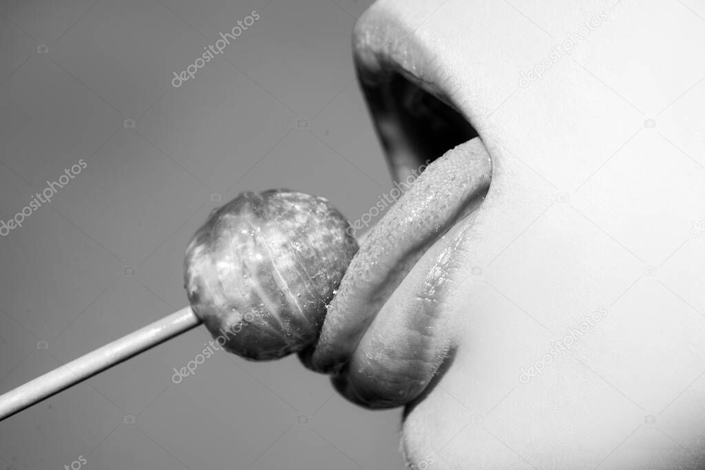 Licking tongue lips. Girl with sexy mouth eating chupa chups close up. Woman lips sucking lollypop. Woman holding lollipop in mouth, close up. Red lips, sensual and sex shop concept.