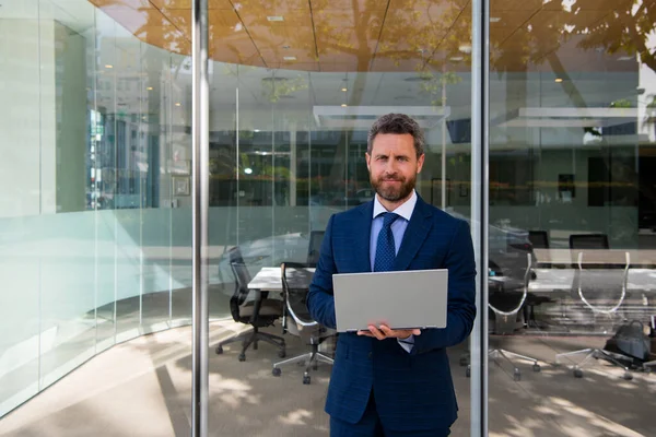 Geschäftsmann mit Laptop steht auf der Straße in der Nähe eines Bürogebäudes. — Stockfoto