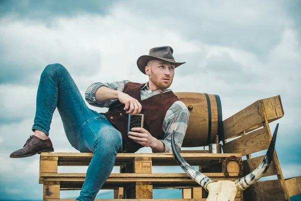 Uomo occidentale sexy con cappello da cowboy. Uomo attraente con whisky o brandy. — Foto Stock