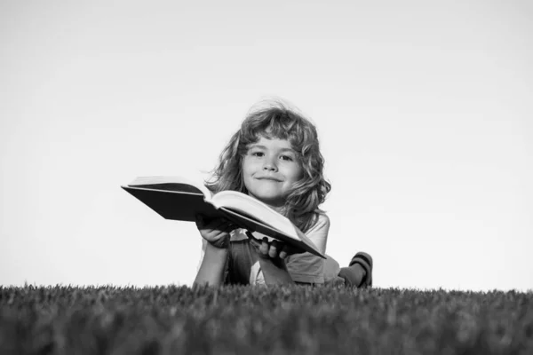 Pojke barn läsa bok, ligga ner på grönt gräs. Barn äventyr, frihet och bekymmerslösa barn. — Stockfoto
