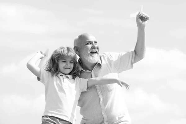 Großvater und Sohn spielen mit Spielzeugpapierflugzeug vor sommerlichem Himmel. Junge mit Träumen vom Fliegen. Familienbeziehung Großvater und Kind. — Stockfoto