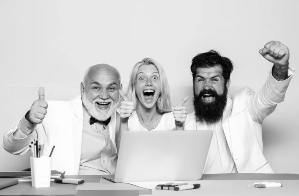 Возбужденные деловые люди сидят за рабочим столом с группой коллег, работающих за ноутбуком. Деловые люди наслаждаются успехом. — стоковое фото