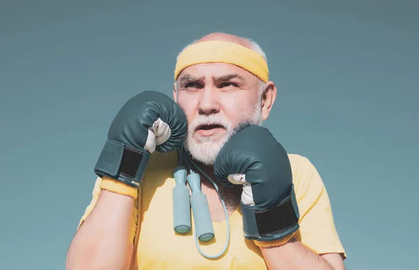 Handsome elderly man practicing boxing kicks - close up portrait. Healthy fighter senior old man boxing gloves. Grandfather doing boxing training in morning.