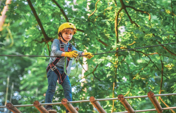 Kids boy adventure and travel. Adventure climbing high wire park. Early childhood development. Cute child in climbing safety equipment in a tree house or in a rope park climbs the rope — Stock Photo, Image