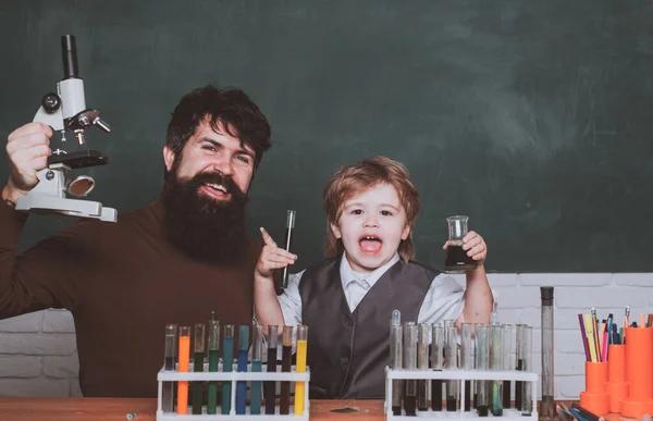 Pequeño niño científico ganando química en el laboratorio de la escuela. Experimentos de biología con microscopio. El hombre enseña a los niños. Papá y su hijito listos para la escuela. Concepto escolar. — Foto de Stock