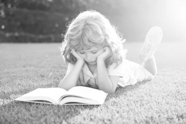 Smarta barn. Pojken läser en intressant bok i trädgården. Sommartid kul. Söt pojke som ligger på gräset och läser en barnbok. Begreppet barns lärande, studier, skola och uppmärksamhet. — Stockfoto