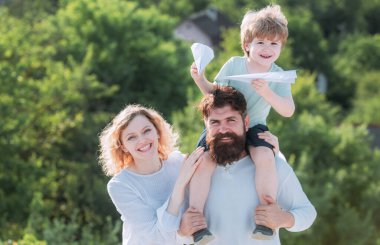 Baba, anne ve oğlu gökyüzü arka planında oynuyorlar. Mutlu bir çocuk ve anne babası yaz mevsiminde arka planda oyuncak kanatlarla oynuyorlar. Baba, anne ve bebek dışarıda birlikte oynuyorlar..