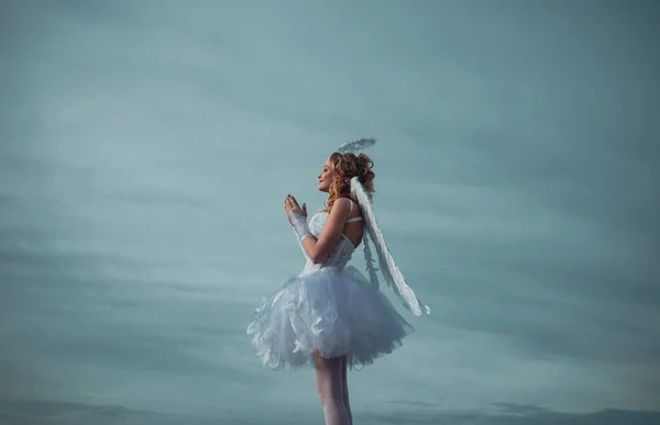 Angel szárnyak baba imádkozni. Szerelmi koncepció. Aranyos tini Cupido a felhő-ég háttérben. Angyal gyermek lány göndör szőke haja-ártatlan lány fogalmát. Imádkozni. — Stock Fotó