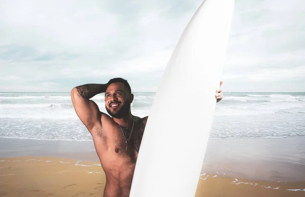 Heureux touriste souriant et tenant planche de surf à beau fond océanique ondulé. Joyeux homme souriant amateur de sport nautique. Activité sportive, voyage et mode de vie heureux concept. — Photo
