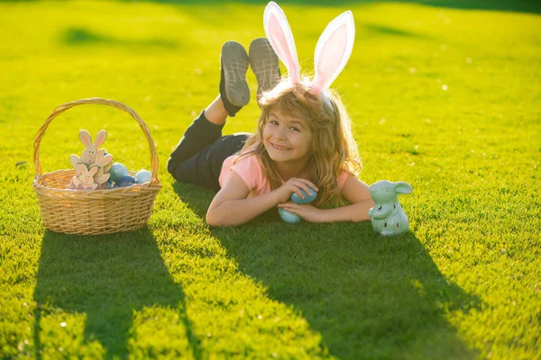 春天公园里，身穿兔子服装、长着小兔子耳朵的小男孩在草地上猎取复活节彩蛋。兔子耳朵里的孩子在花园里打猎复活节彩蛋. — 图库照片