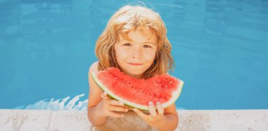 Çocuk havuzda karpuz yiyor. Kumsalda kırmızı karpuz yiyen tatlı çocuk, mavi suya karşı beyaz çocuk karpuz yiyor..