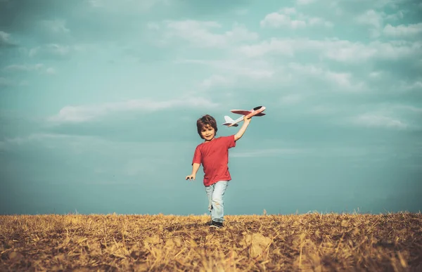 Recuerdos de la infancia: hermoso cielo sobre el prado. Concepto de imaginación de ensueño infantil. Niño activo jugando. Niño jugando con juguete avión sobre prado divertirse y sonreír . — Foto de Stock