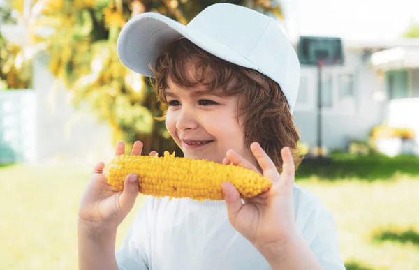 Rapaz a divertir-se com comida legumes milho. Criança no jardim, milho - menino adorável comendo milho na espiga no jardim . — Fotografia de Stock