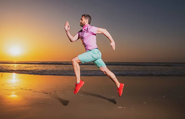 Een man die bij zonsondergang op het strand rent. Een jogger op de vlucht. Dynamisch springen. Sportsprong. — Stockfoto
