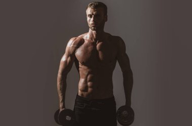Seksi spor gövdesi, dambılı adam. Dambılı bir sporcunun portresi. Stüdyoda kaslı, gömleksiz bir adam var..
