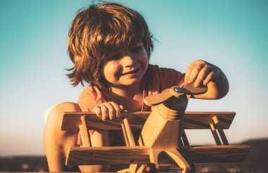 Çocuk seyahat etmeyi ve bir uçak pilotuyla oynamayı hayal ediyor. Mutlu çocuk mavi gökyüzü arka planında oyuncak uçakla oynuyor..