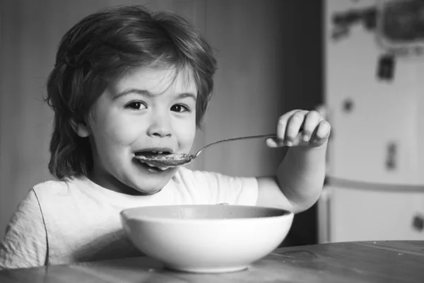 Barnet i köket vid bordet äter. Grabben äter. Glada barn, ät frukost. Mat och dryck för barn. Skrattar söt barn baby pojke sitter i barnstol och äter på suddig bakgrund — Stockfoto