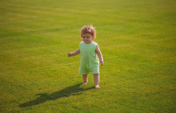 Malé děťátko se učí šplhat po trávě. Pojem děti měsíce. Happy child playing on green grass playground. — Stock fotografie