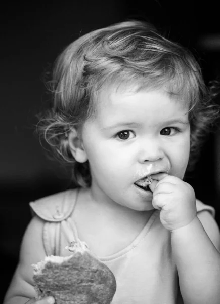 Portrait of cute baby with bread in her hands eating. Cute toddler child eating sandwich, self feeding concept. — Stock Photo, Image
