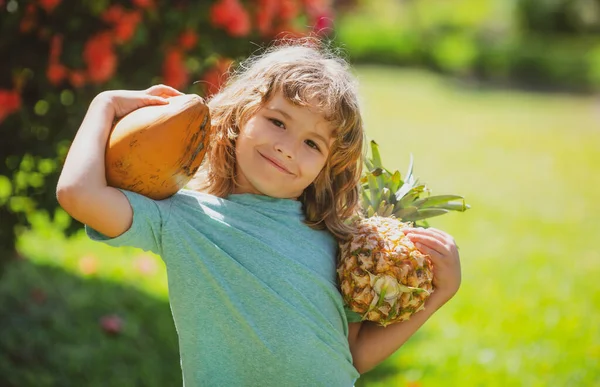 Tropik bahçede ananaslı ve hindistan cevizli şirin çocuk. Çocuklar için taze tropikal meyveler. Taze organik tropikal meyvelerle sağlıklı bir yaşam tarzı.. — Stok fotoğraf