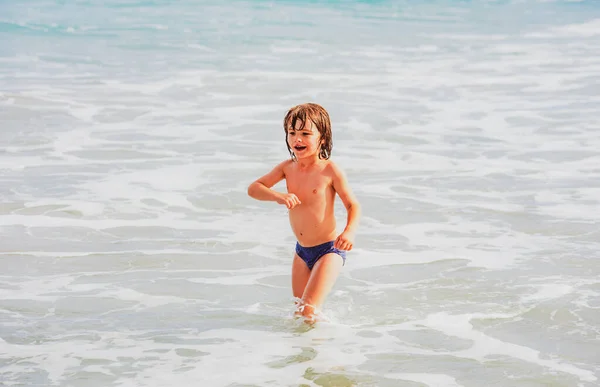 子供の男の子は夏休みにビーチで遊んでいます。美しい海と自然の中で子供たち。水上を走る海辺の休暇で幸せな子供たち. — ストック写真