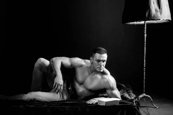 Sexy knappe jongeman die zonder shirt in bed ligt, een boek leest. Een knappe intellectueel. — Stockfoto