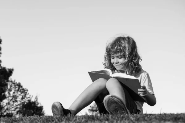 Menino inteligente leitura livro no parque ao ar livre. — Fotografia de Stock