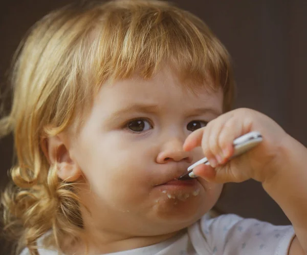 Милое детское лицо с ложкой и тарелкой на кухне дома. — стоковое фото