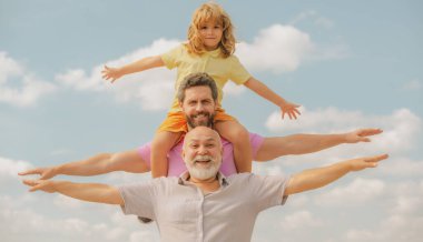 Baba, oğul ve büyükbaba mutlu çoklu nesil aileleri, elleri havada ya da gökyüzünde uçan kolları açık. Nesiller boyu erkekler.