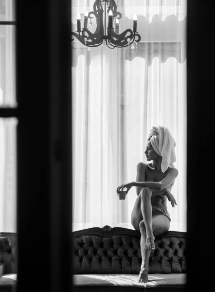 하얀 목욕 가운을 입고 수건을 쓴 젊고 아름다운 여성들이 깨어나자마자 침실에서 커피를 마십니다. 아파트나 호텔 방의 침대에 누워 있는 조심성 있는 여성 모델. 좋은 아침 휴식. — 스톡 사진