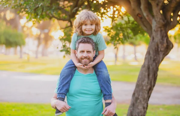 Heureux père et fils profitant de l'heure d'été en vacances dans un parc ensoleillé. Papa portant sur les épaules heureux petit garçon. — Photo