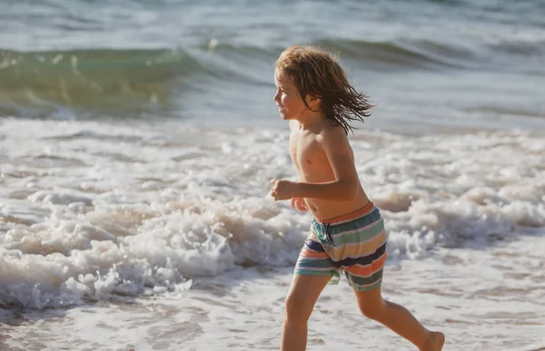 Bambino che corre attraverso l'acqua vicino alla riva lungo la spiaggia del mare. Un ragazzo corre lungo la costa del mare. Resto dei bambini in vacanza estiva. — Foto Stock