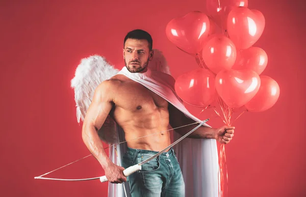 Mooie sexy engeltjes. Valentijnsdag. Een gespierde man die zich voordoet als engel. Cupido in liefde met kleurrijke ballonnen en pijl en boog. Vriendje op rode achtergrond. — Stockfoto