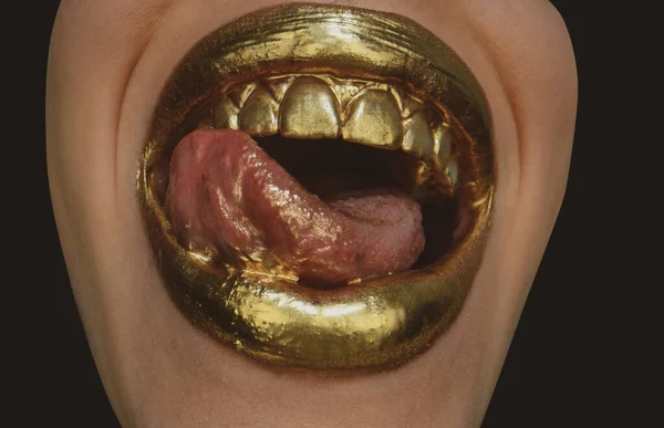 Luxury gold lips make-up. Golden lips with golden lipstick. Gold paint on lips of sexy girl. Sensual woman mouth, isolated background. Sexy tongue. Sensual lick.