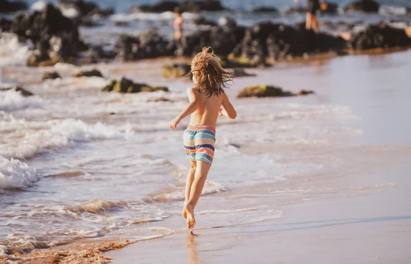 Вид сзади мальчика, прыгающего и бегающего на морском пляже. — стоковое фото