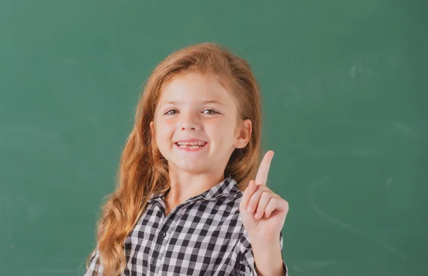 Retrato de alumna nerd escolar con expresión sorprendente apuntando con el dedo contra pizarra. —  Fotos de Stock