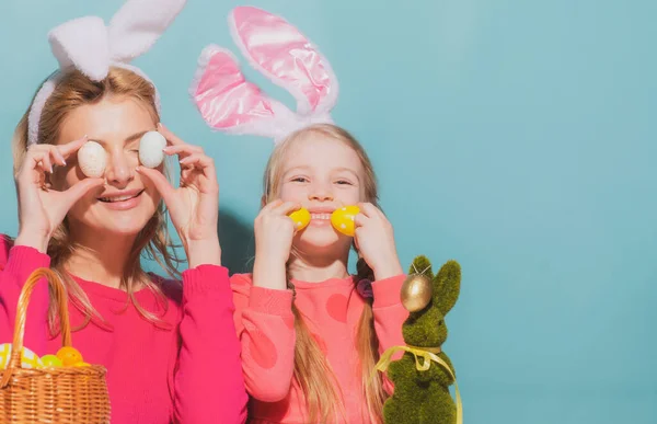 Retrato de madre con hija con orejas de conejo decorando huevos de Pascua aislados en azul. —  Fotos de Stock