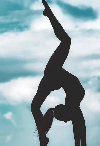 Ragazza silhouette ginnica sul cielo. Giovane ragazza snella che fa acrobazie acrobatiche. Ginnasta in retroilluminazione. — Foto Stock