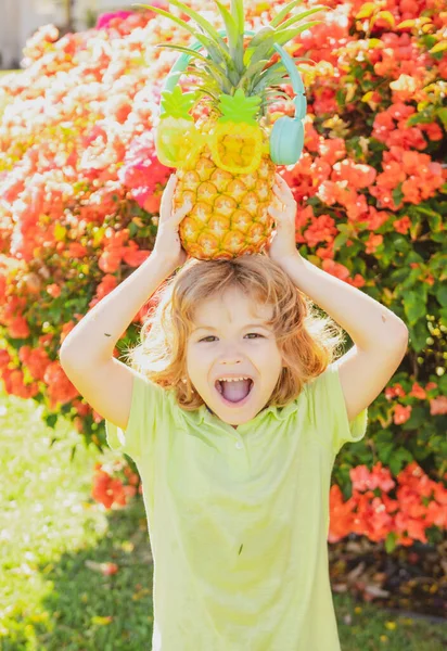 Little blonde kid hugging pineapple on nature background. Childhood, healthy nutrition, advertising. Close up kids funny face, copy space. — Stock Photo, Image
