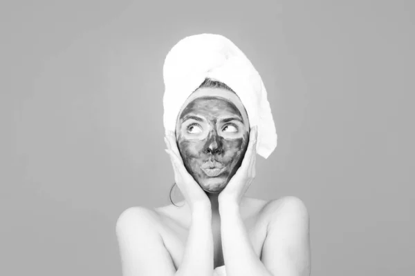 Joven mujer hermosa en una máscara para la cara de la arcilla negra terapéutica. Tratamiento de spa. Procedimiento facial de barro cosmético, concepto de salud del spa. Tratamiento de belleza del cuidado de la piel. Toalla en la cabeza. Barro médico. — Foto de Stock