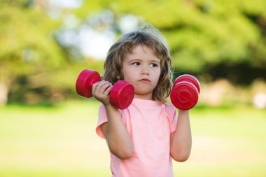 Dambılı sportif çocuk. Çocuklar spor ve spor, sağlık ve enerji. Sağlıklı çocuk yaşam tarzı. Neşeli çocuk halterlerle egzersiz yapıyor. Çocuk, dambıllarla egzersiz yapıyor. Spor portresi çocuklar..